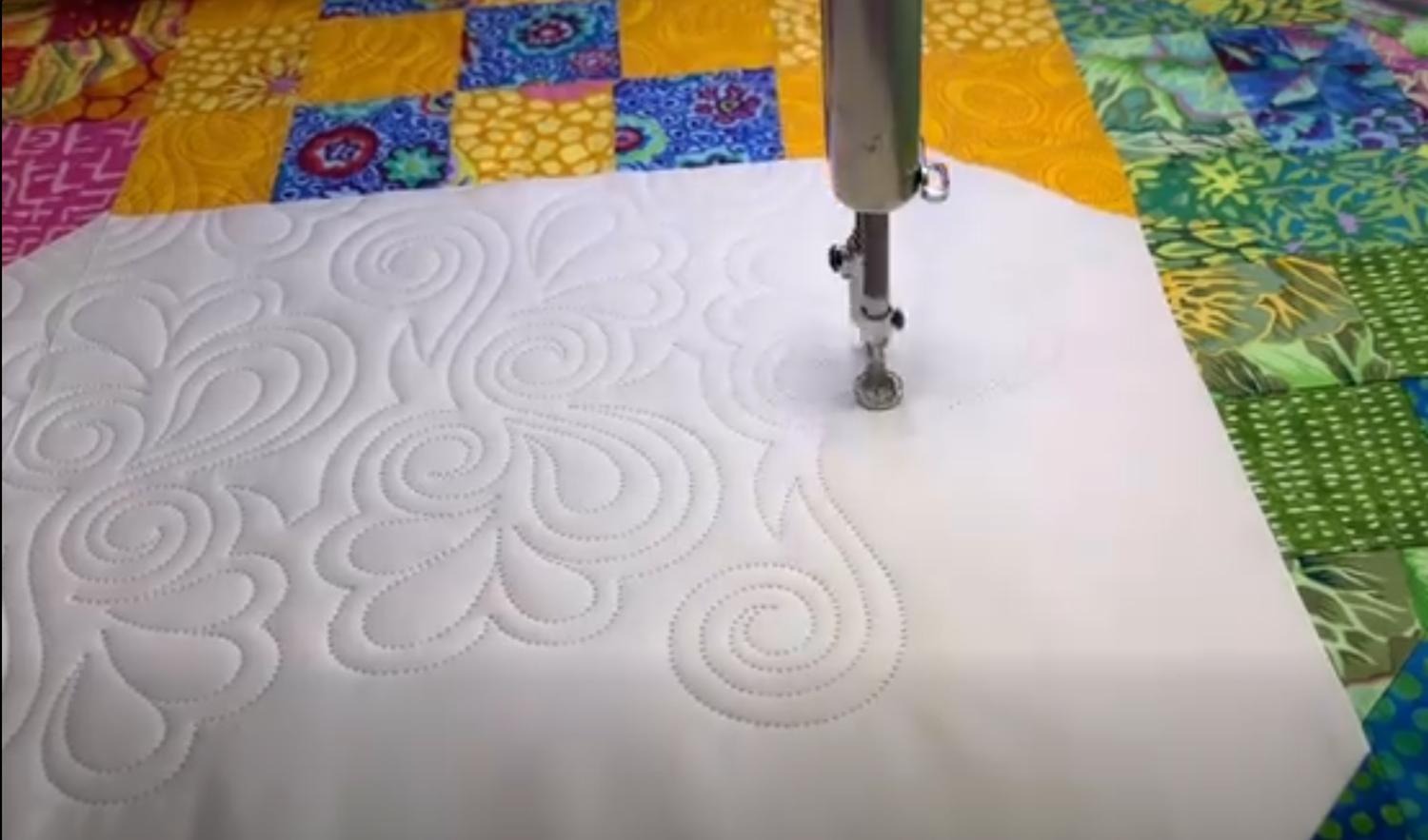 Longarm machine in action — the quilting head stitching a detailed pattern across a loaded quilt